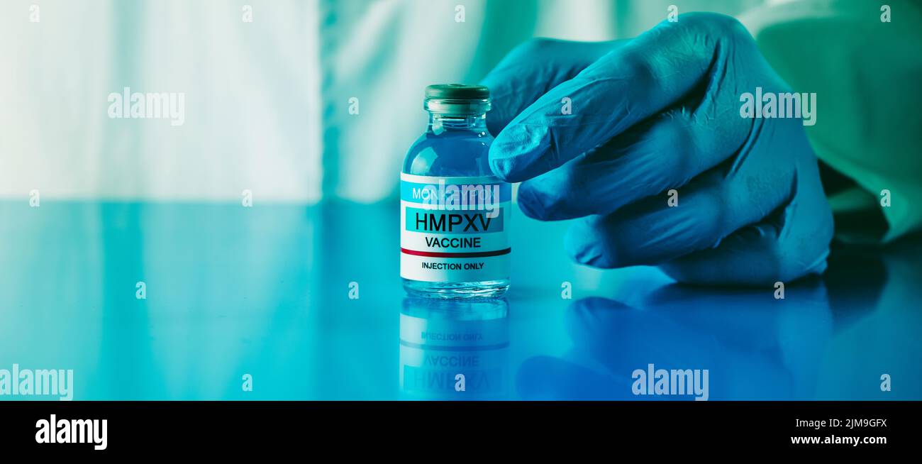 a healthcare or laboratory worker, wearing blue surgical gloves, shows a simulated vial of monkeypox vaccine, in a panoramic format to use as web bann Stock Photo