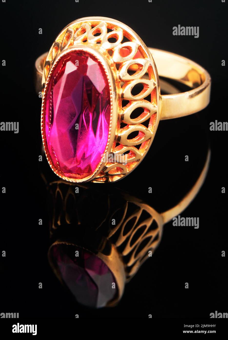 Golden finger ring with pink precious stone on black mirrored surface Stock Photo