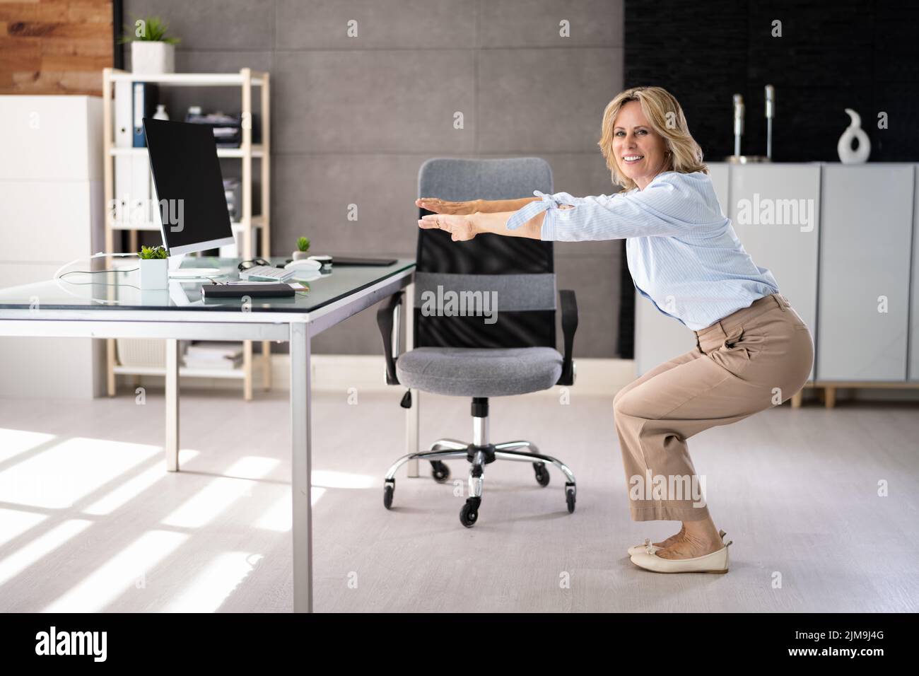 Female Doing Office Yoga Exercise Sit Up And Stretch At Desk Stock Photo