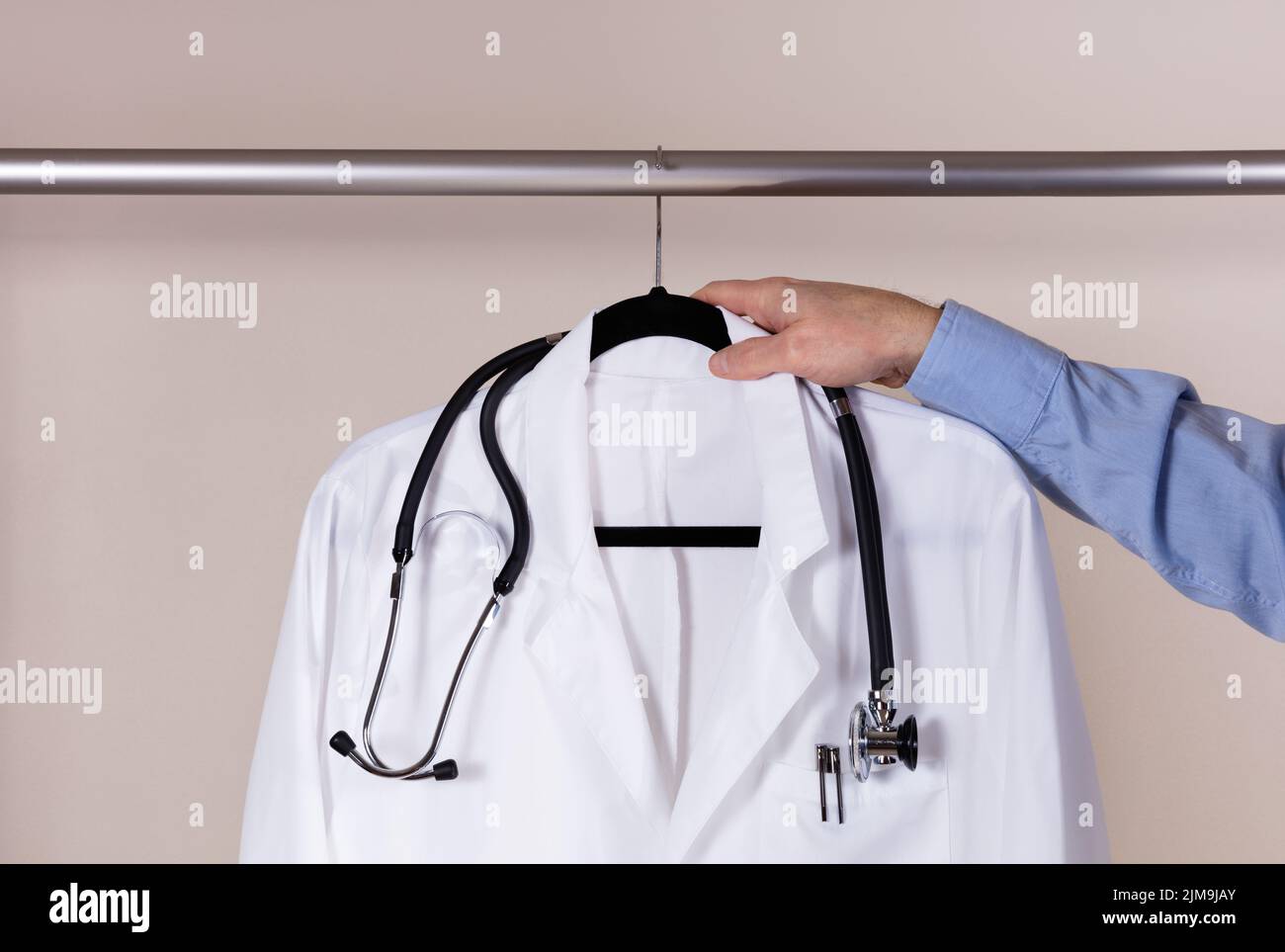 Medical white consultation coat with stethoscope being taken off rack by male doctor hand Stock Photo