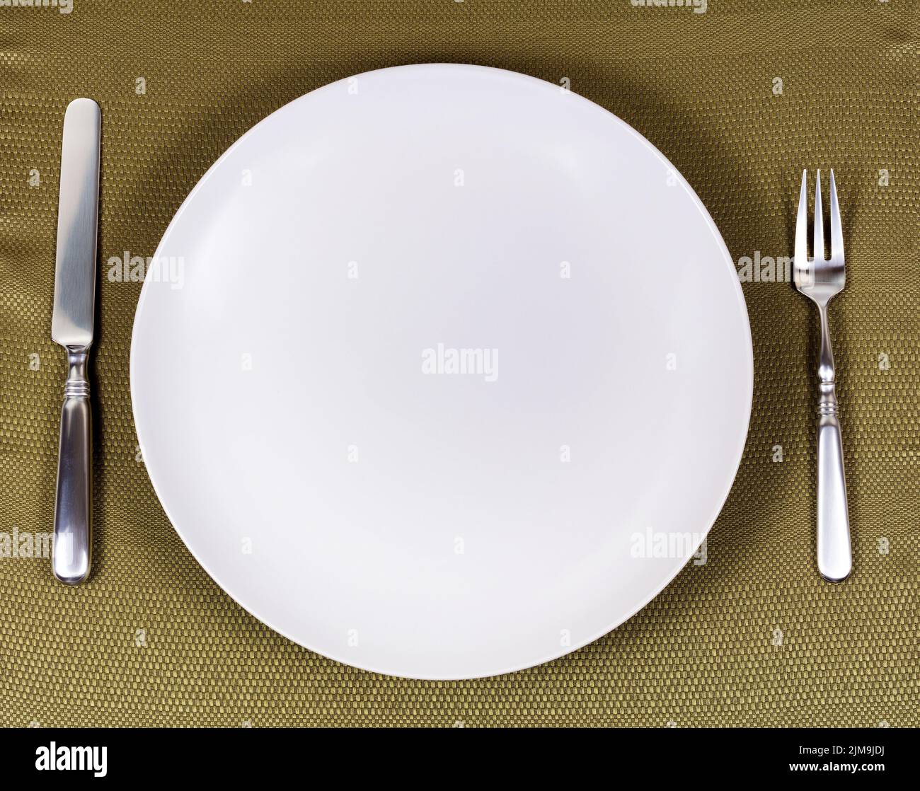 Simple white plate with silverware for dinner setting on table cloth Stock Photo