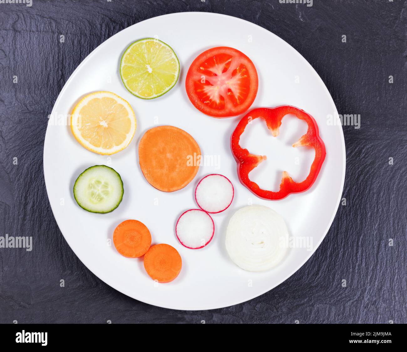Circle of sliced fruit and vegetables in white plate on natural slate stone background Stock Photo