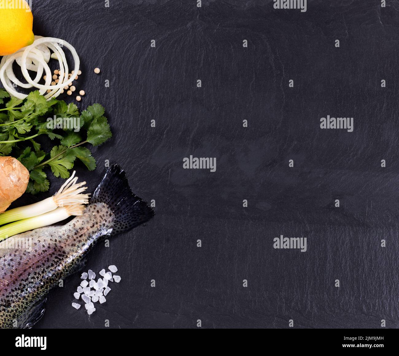 Fresh whole fish and herbs displayed on natural slate stone background