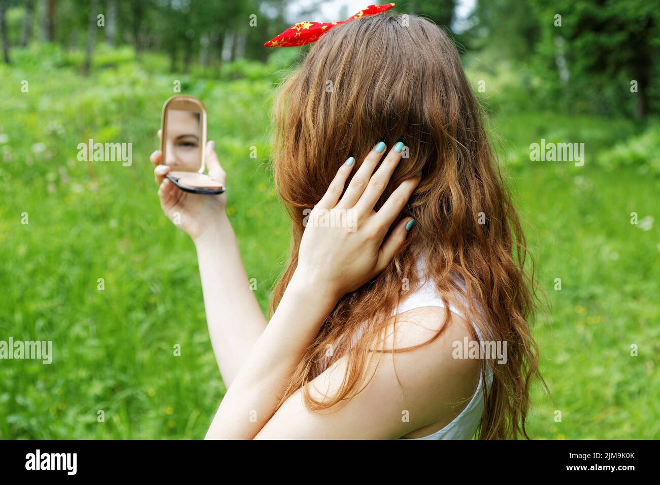 Girl with a bow on her head looking into the mirror on the nature Stock Photo