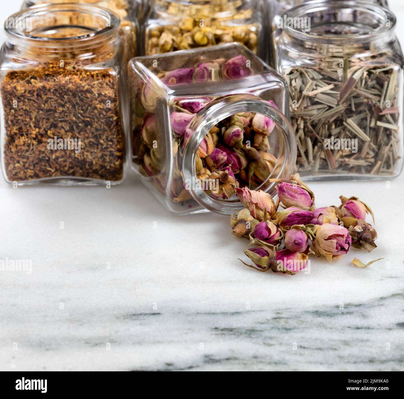 Spices and herbs in small glass jars pouring onto white marble stone