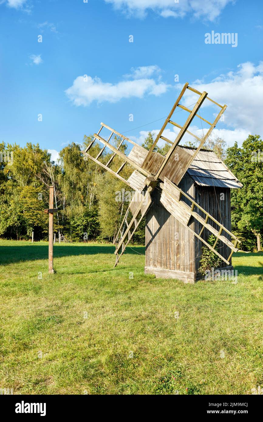 A wooden old windmill and a cross stand on a green meadow on a sunny day and clear weather against a blue sky. Copy space, vertical image. Stock Photo