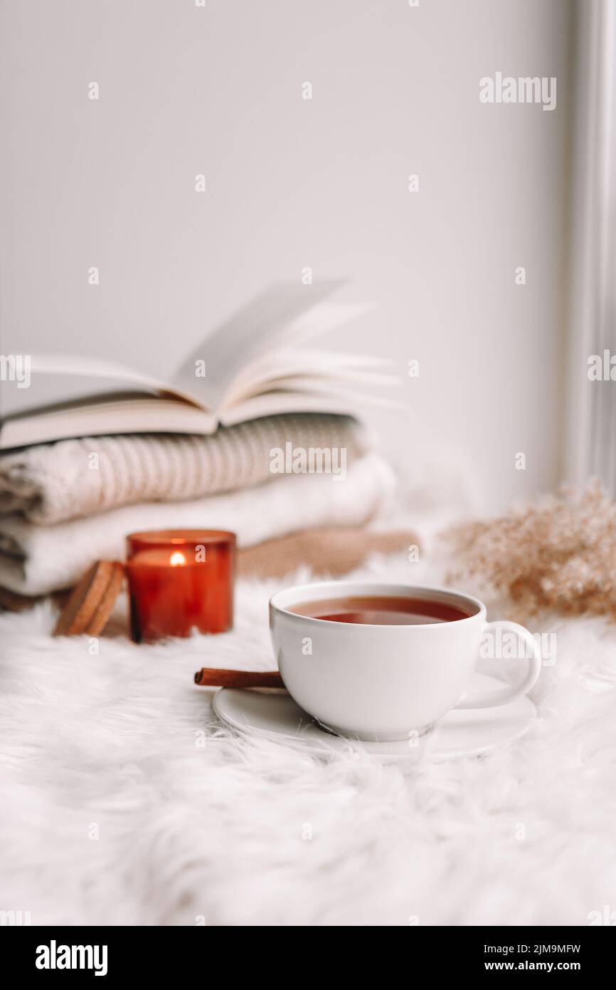 A cup of tea on the window with burning candles and sweaters. Stock Photo