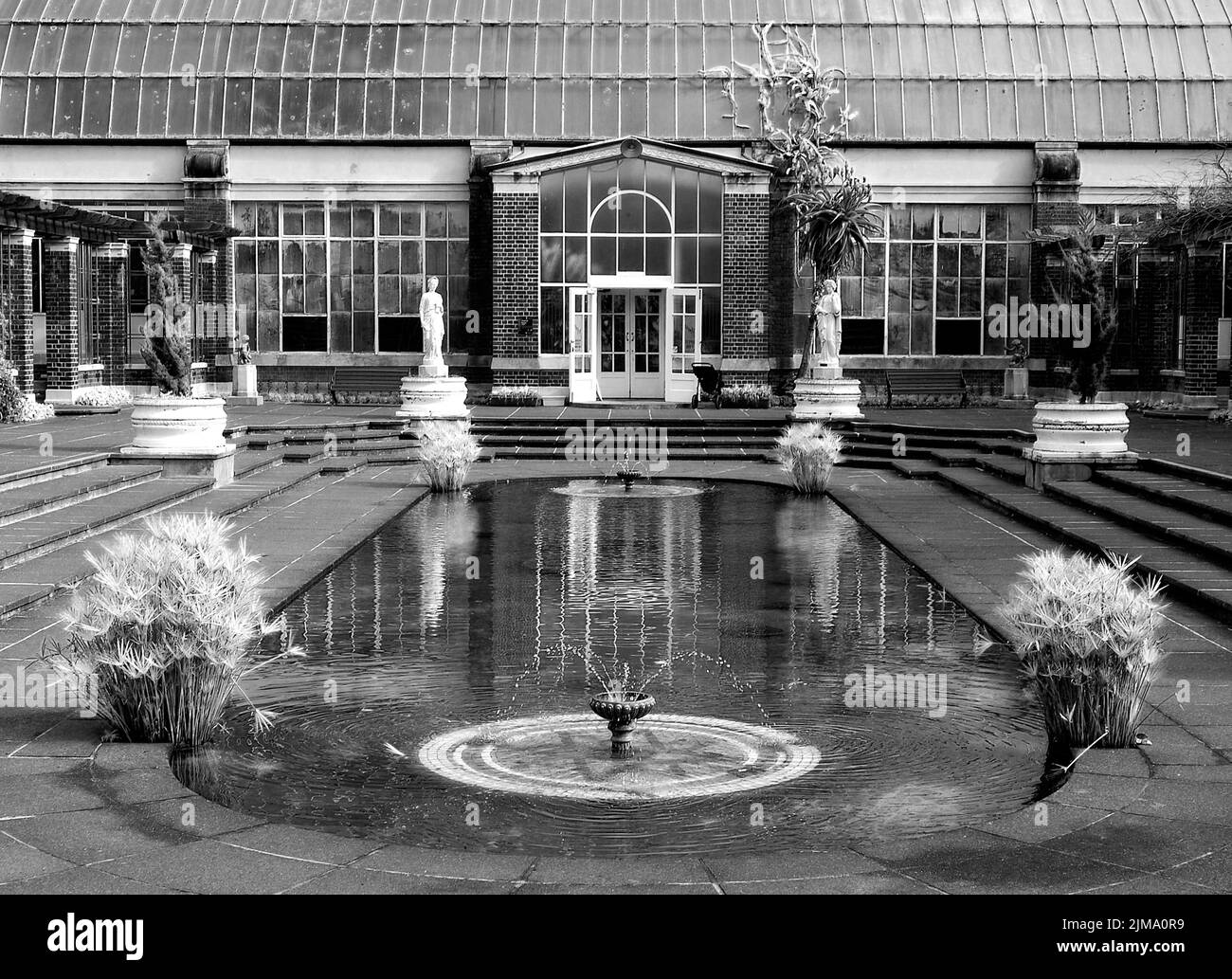 A black and white shot of a garden with a water fountain and sculptures in daylight Stock Photo