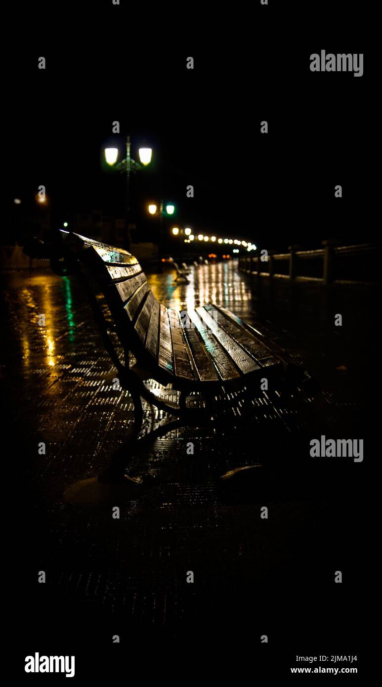 A dramatic scene of a wet wooden bench in a dark park post rain, vertical shot Stock Photo