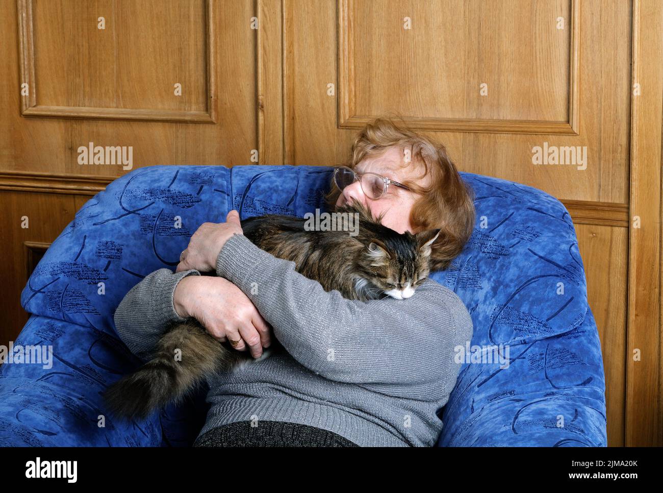 Old woman asleep in a chair in an embrace with a cat Stock Photo