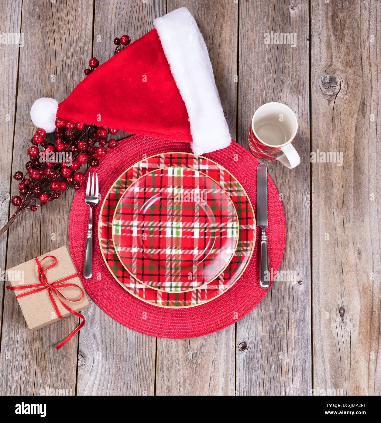 Xmas dinner setting with gift box and Santa cap on rustic wooden boards Stock Photo