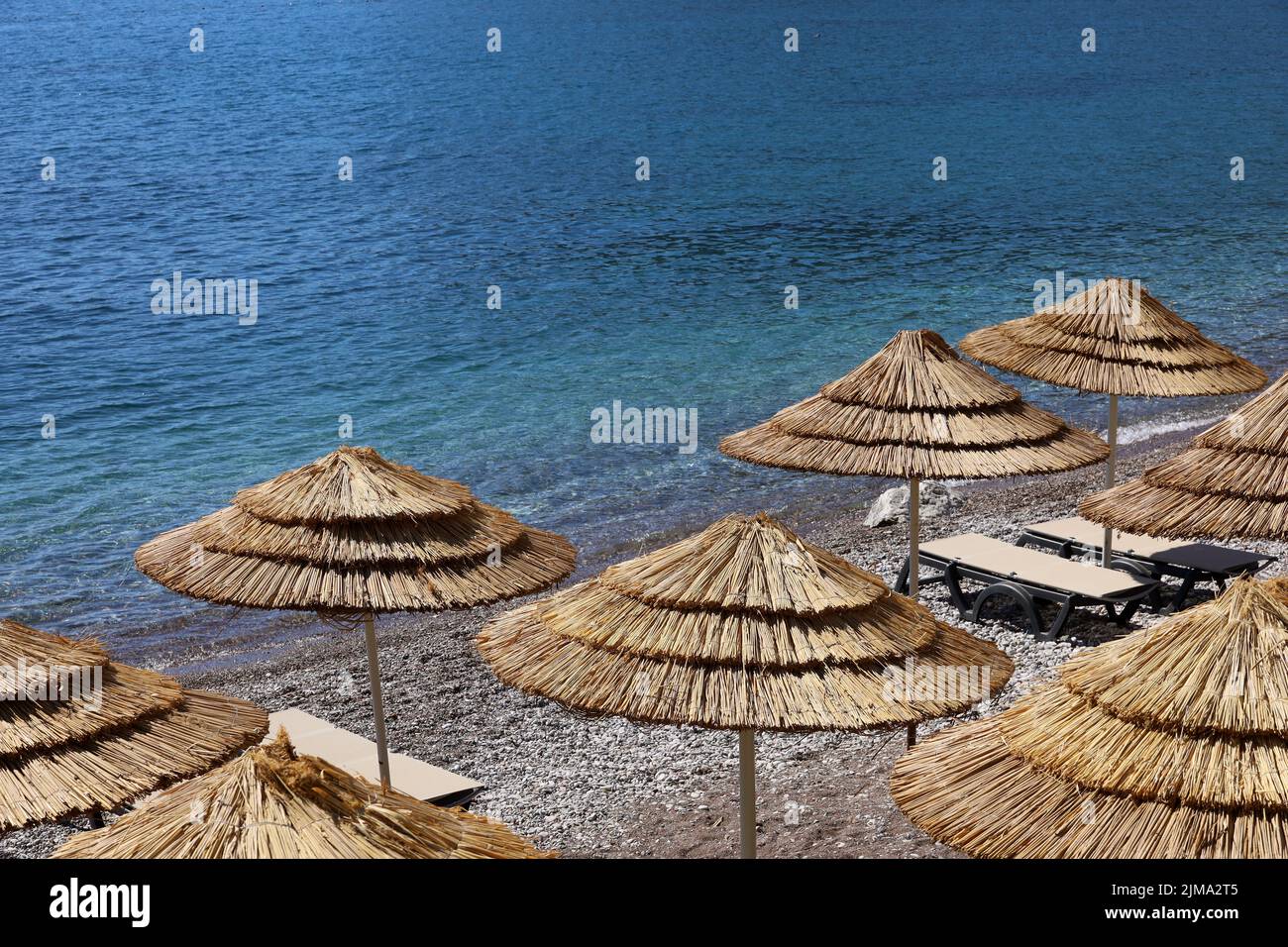 Empty pebble beach with wicker parasols and lounge chairs. Picturesque view to sea with blue water, summer resort Stock Photo