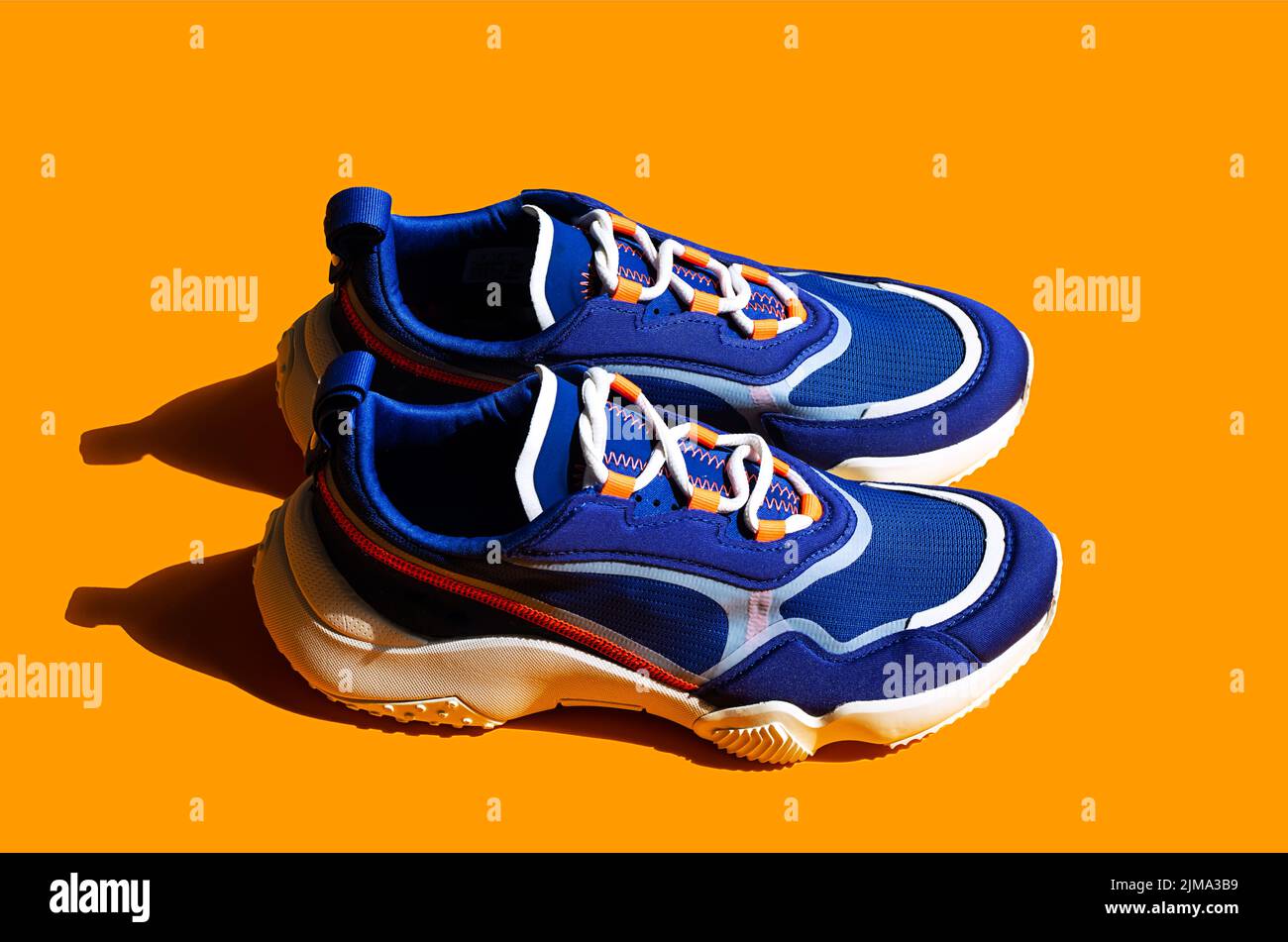Blue sneakers on orange background. Trendy sport shoe, street casual footwear. Stock Photo