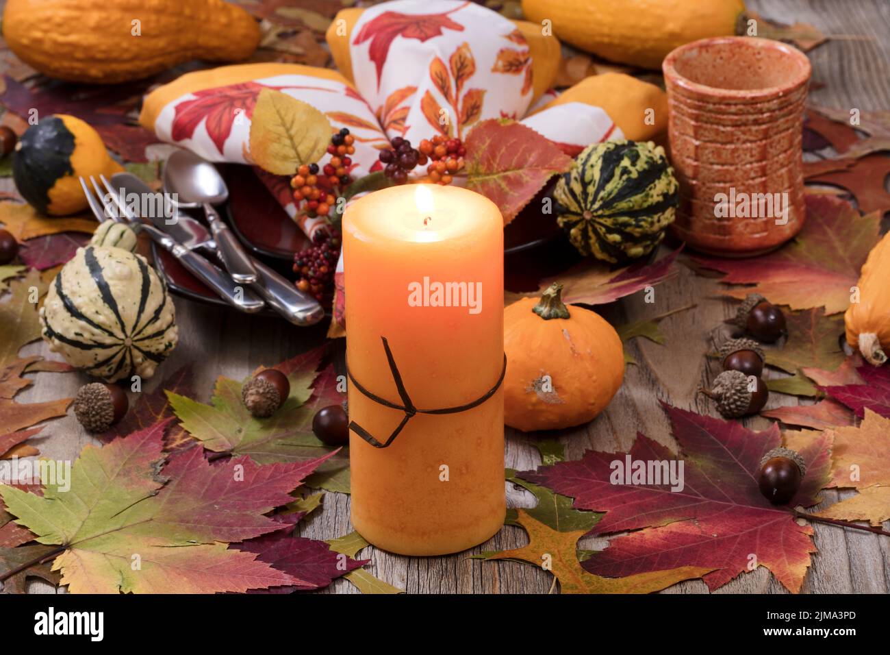 Holiday candle glowing for dinner setting for fall season with real gourd decorations and leaves Stock Photo