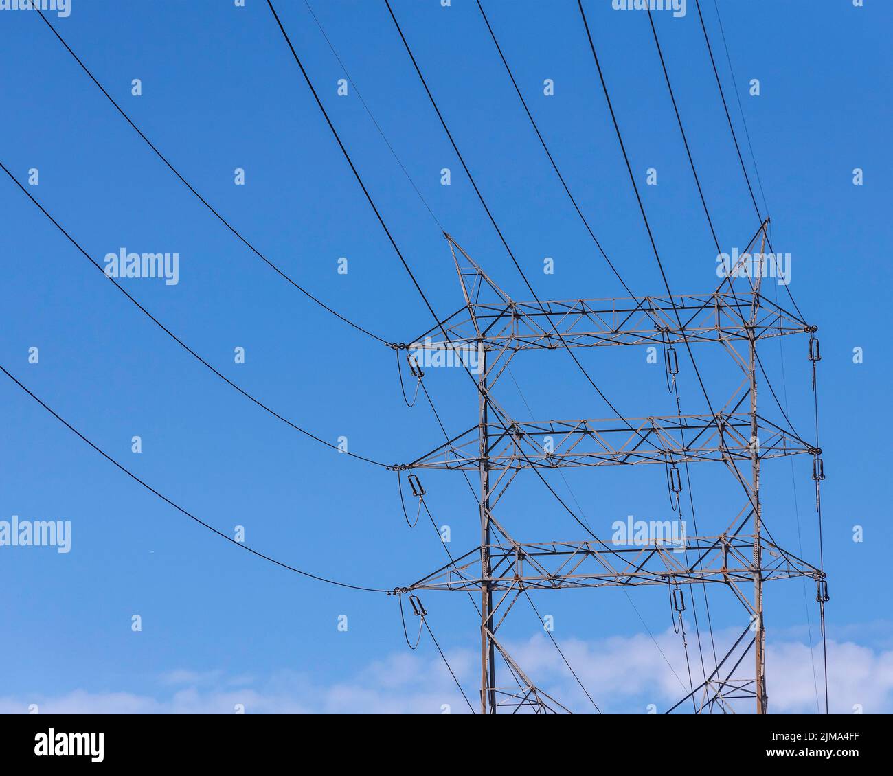 A steel lattice transmission tower stands against a clear blue sky. Stock Photo
