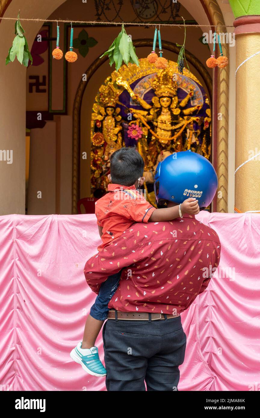 Howrah,India -October 26th,2020 : Father with helmet on, showing Goddess Durga to his child, Durga inside old age decorated home. Durga Puja. Stock Photo