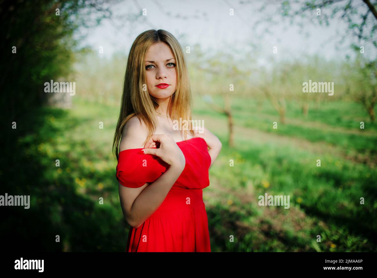 Portrait of light hair girl on red dress background spring garden. Stock Photo