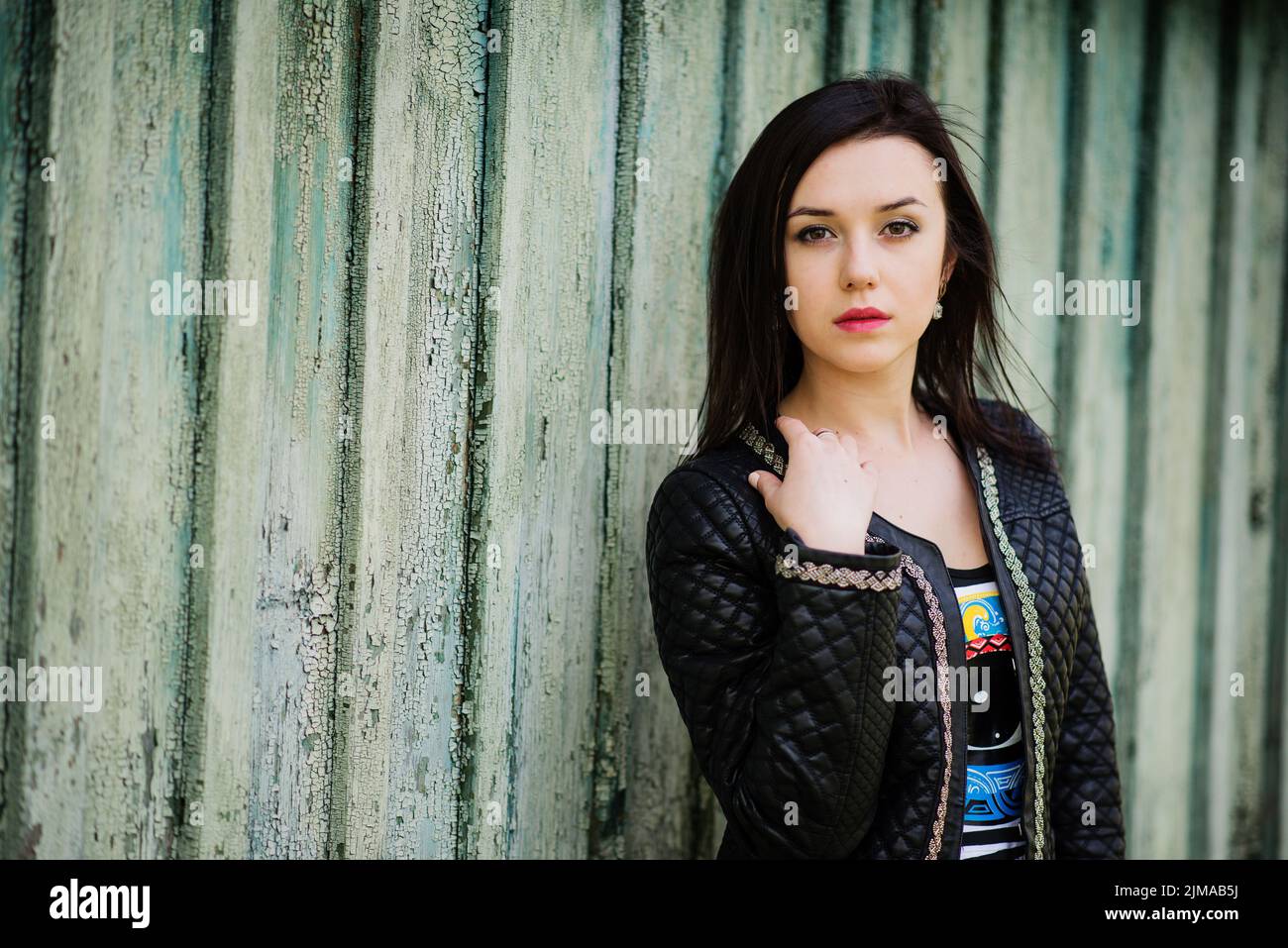 Brunette model girl at leather jacket posed background old wooden house. Stock Photo