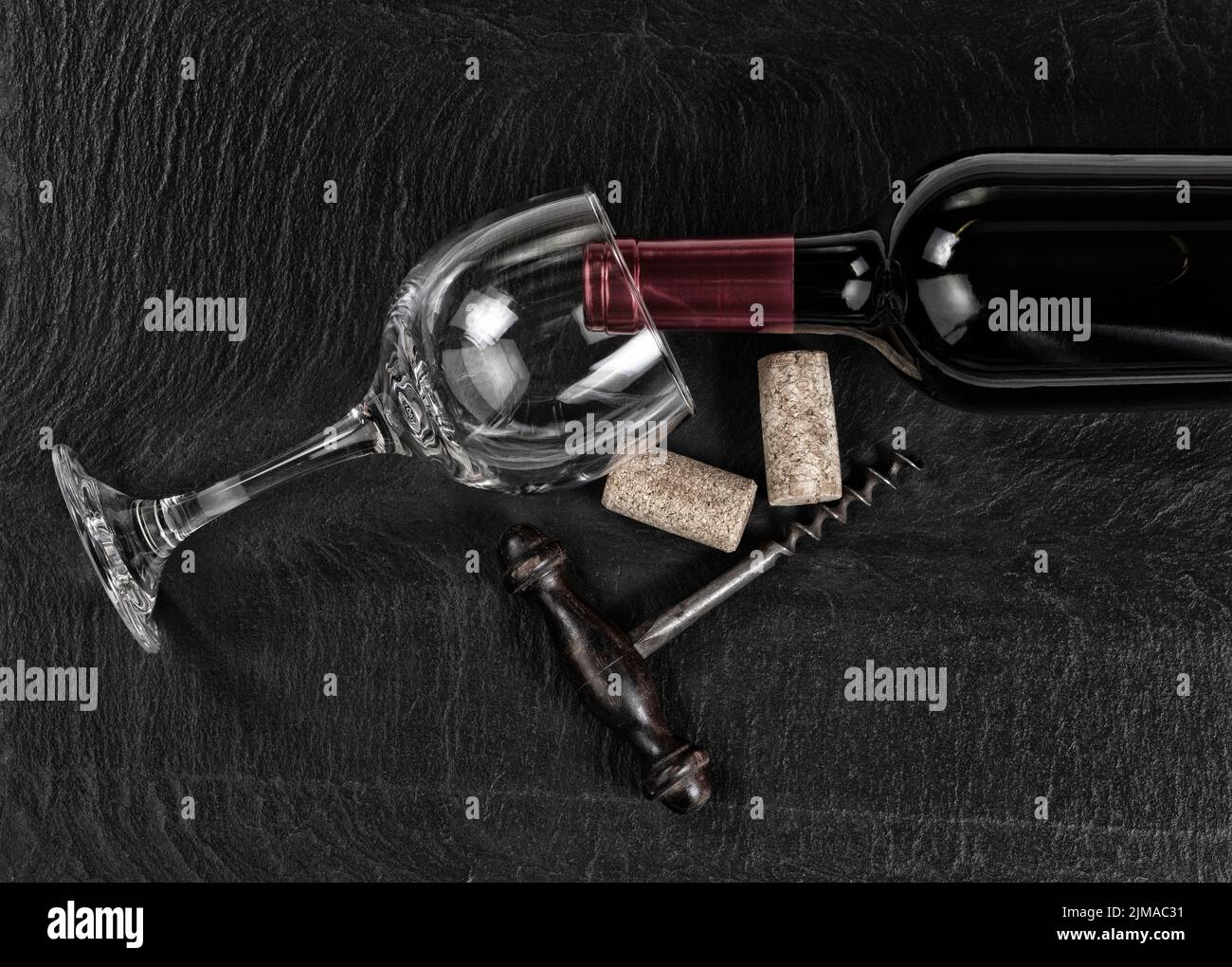 Overhead view of vintage corkscrew with red wine bottle and glass on black slate background Stock Photo