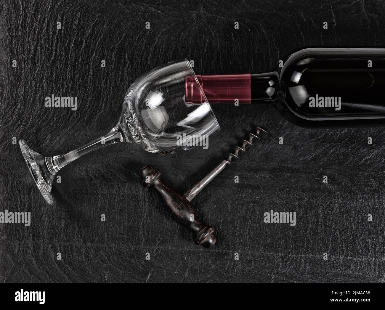Overhead view of vintage corkscrew with red wine bottle and drinking glass on black slate background Stock Photo