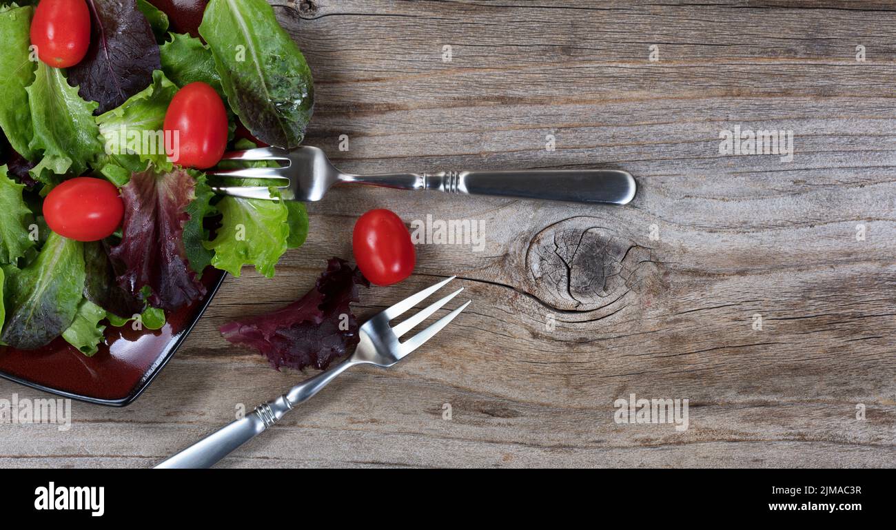 Healthy organic salad flowing out of plate on rustic wooden table background Stock Photo