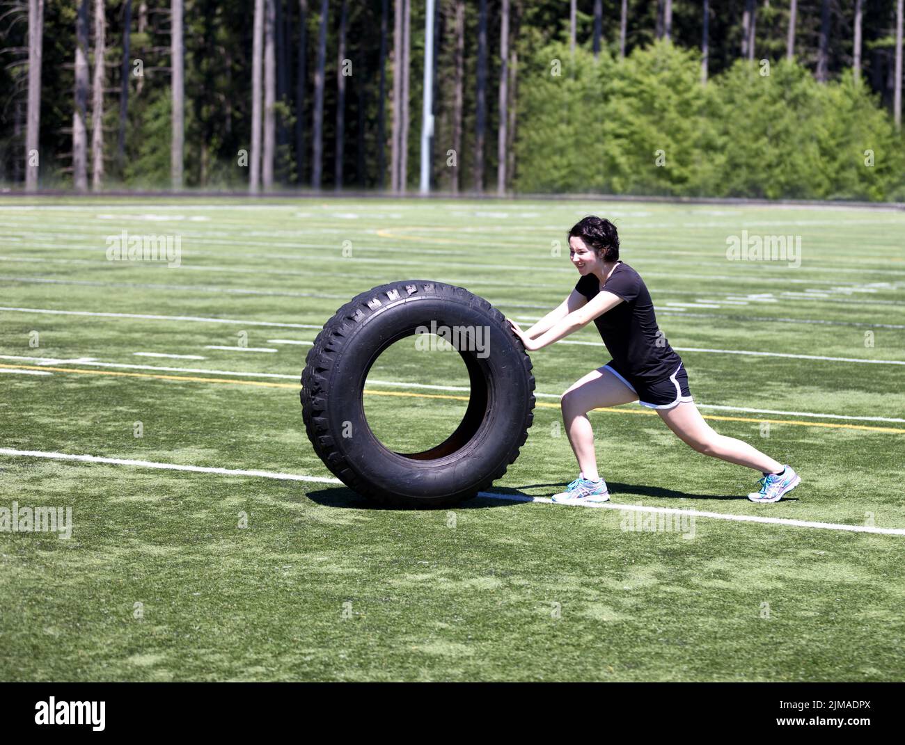 Teen girl pushing heavy tire on sports field during hot day Stock Photo