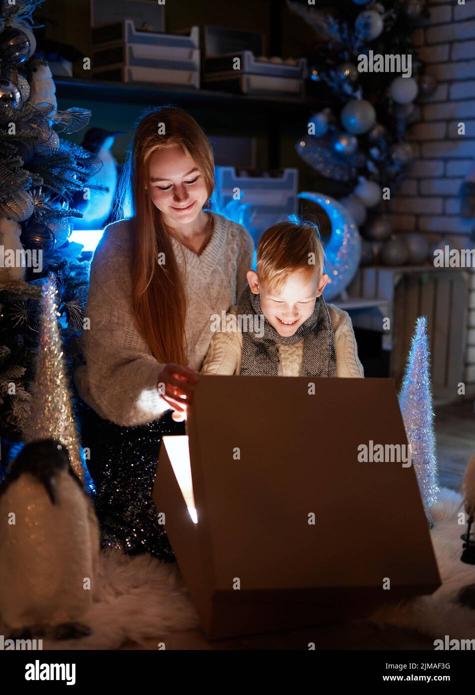Caucasian kids, sister and brother are celebrating winter holidays. Girl and boy opening Christmas gift at decorated home. Christmas. Happiness. High quality vertical image Stock Photo