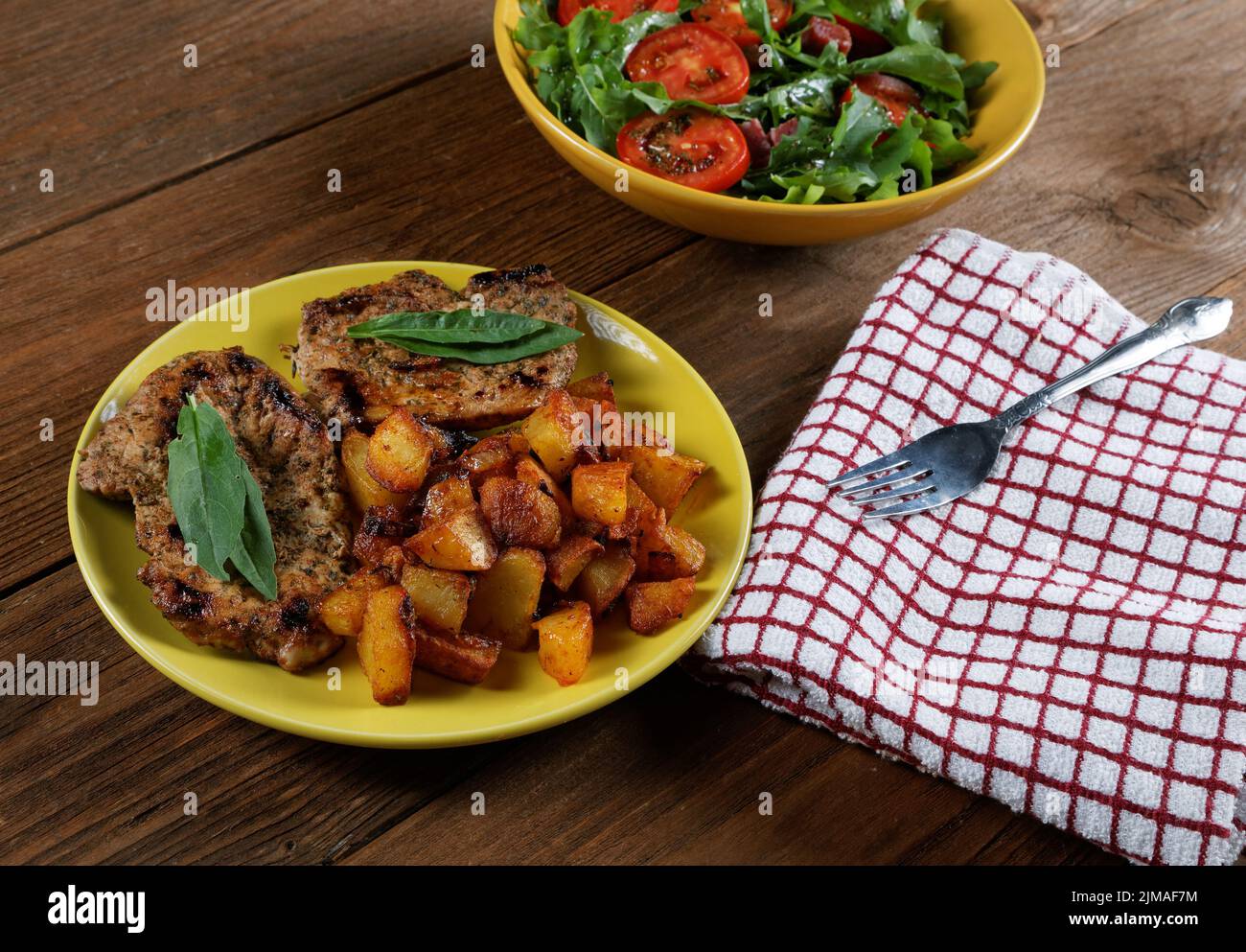 Fried potatoes with meat and a plate of salad on the table Stock Photo