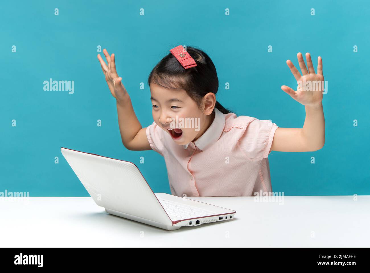 Surprised, Cute asia little girl who enjoy the laptop computer on blue background Stock Photo