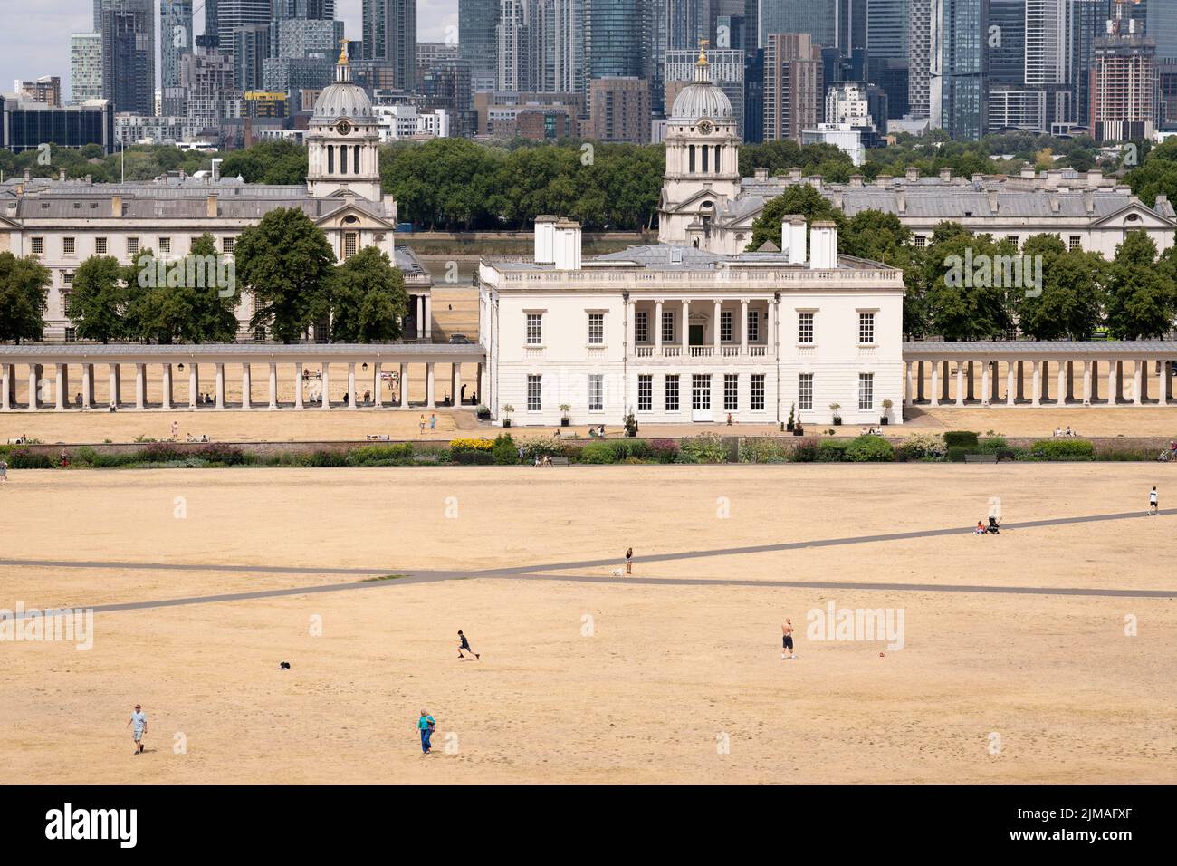 Overlooked by the former royal residence, Queen's House, park users walk through a parched grass landscape in Greenwich Park as the UK's heatwave and drought continues into August with little rain having fallen in London and south-east England, on 4th August 2022, in London, England. Queen's House is a former royal residence built between 1616 and 1635 near Greenwich Palace. Stock Photo