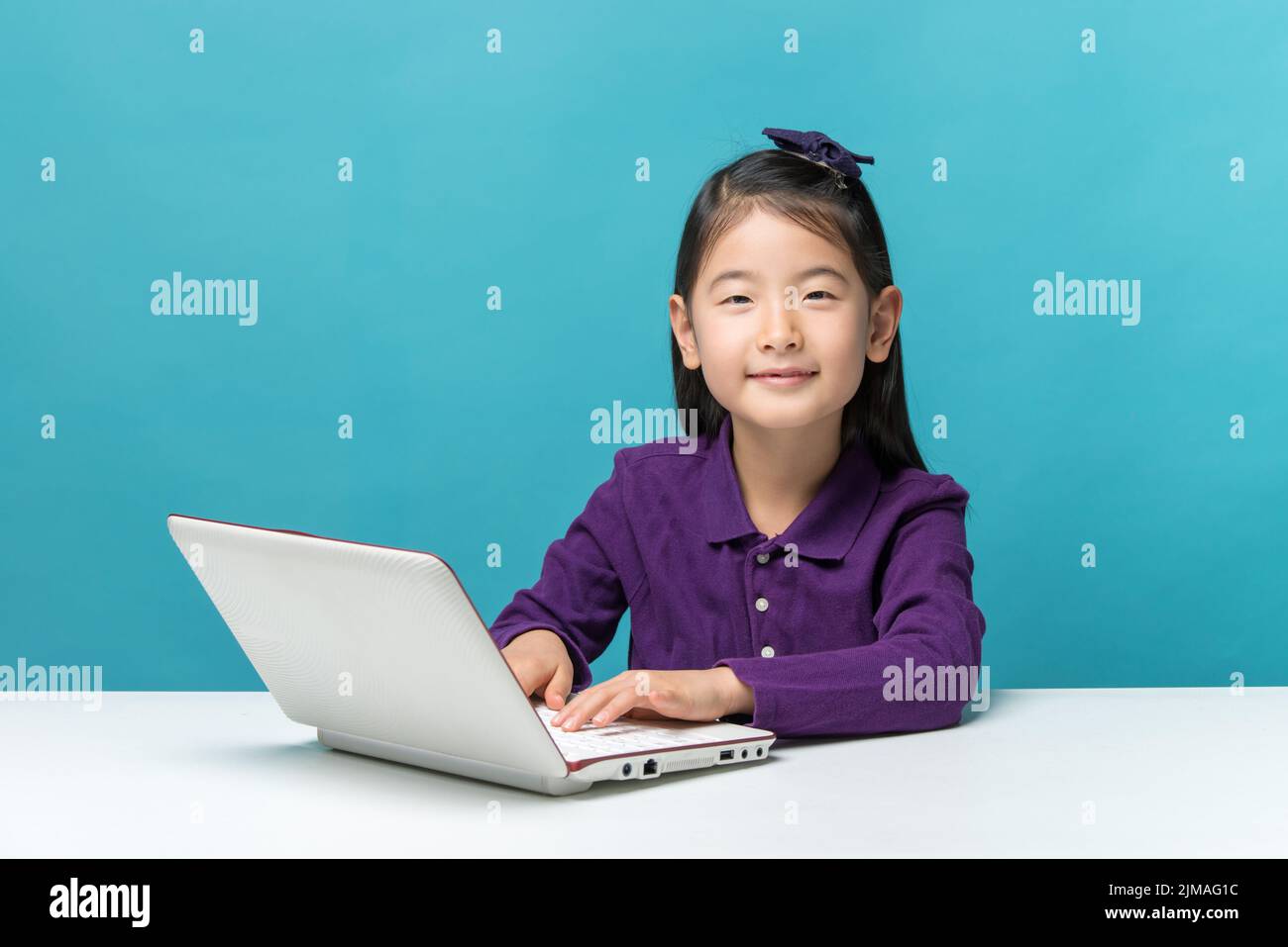 Cute asia little girl who enjoy the laptop computer on blue background Stock Photo