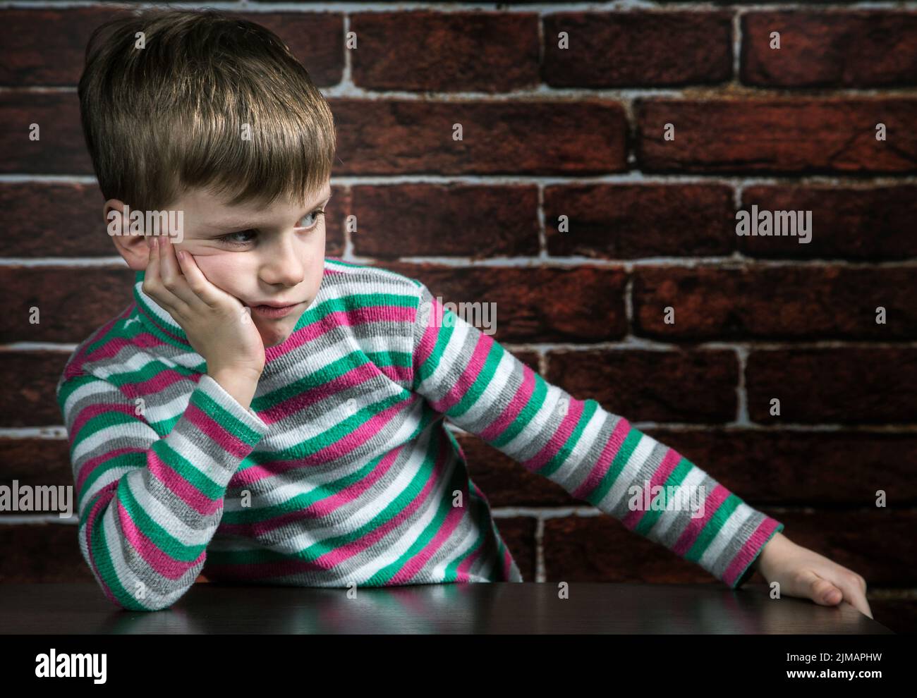 Six year old boy with a thoughtful expression on the wall background Stock Photo