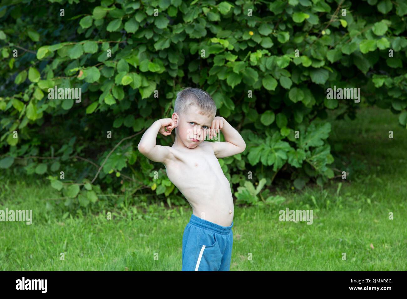 Little boy shows biceps in the garden on a summer day Stock Photo