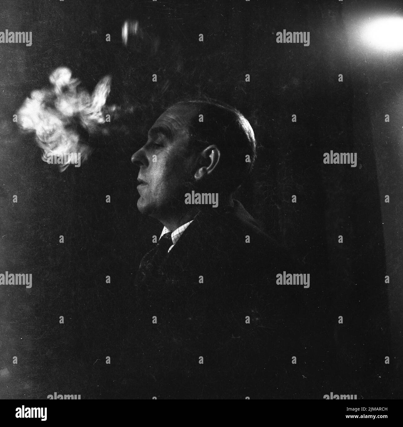1950s, historical, portrait of a gentleman in a shirt & tie sitting with a puff of smoke beside his head, coming from a cigarette - out of picture - he is smoking. Stock Photo