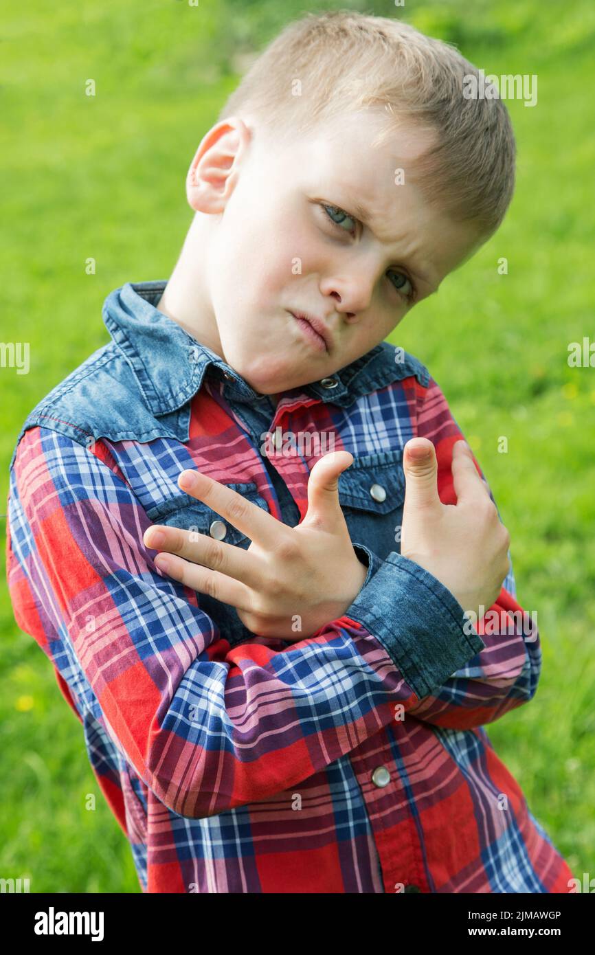 The boy grimaces in the style of rap on the background of green grass Stock Photo