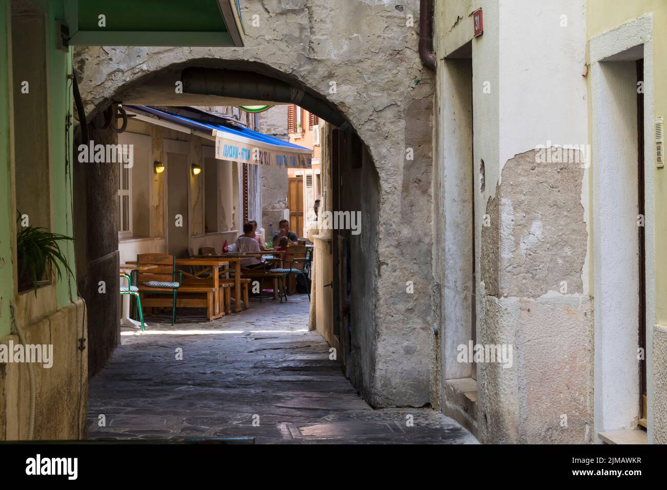 View through an arched gate onto a restaurant terrace in a narrow picturesque street in the historic center of Piran. Slovenia. Stock Photo