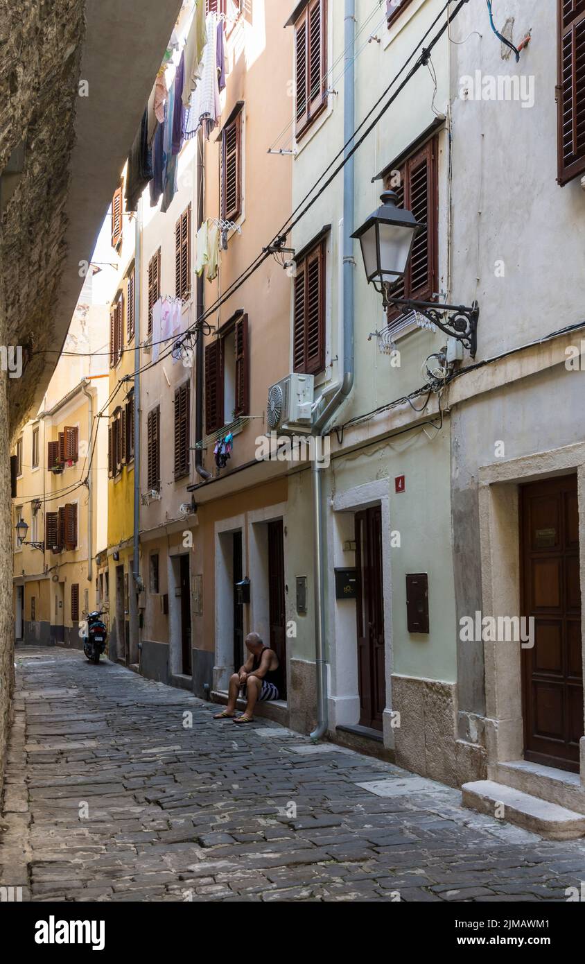 Senior man sitting on the doorstep of his house in a narrow picturesque street in the historic center of Piran. Slovenia. Stock Photo