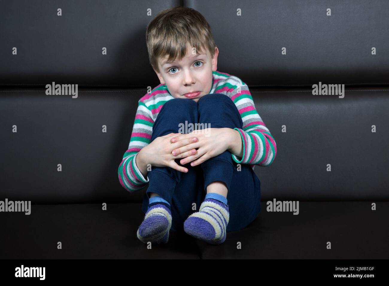 Six-year-old  boy  with a grimace of surprise sits on the couch Stock Photo