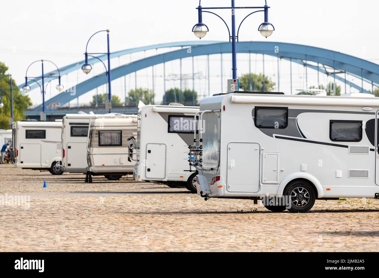 Many white modern campervan recreational motor home vehicles parked in row at camper park site Magdeburg city against Elbe river bridge. Motorhome Stock Photo