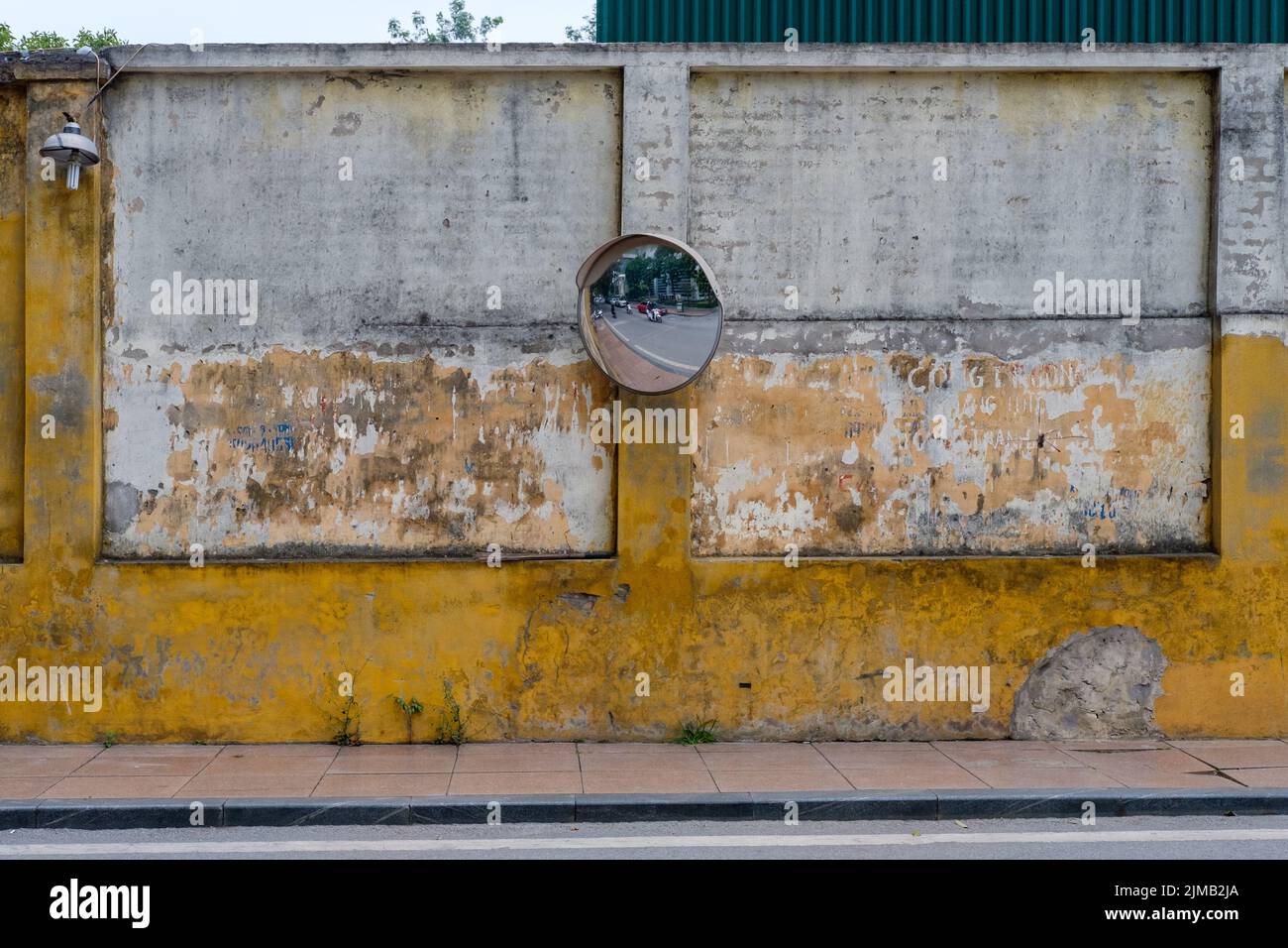 Traffic mirror on a decaying old wall in the streets of Hanoi, Vietnam. Stock Photo
