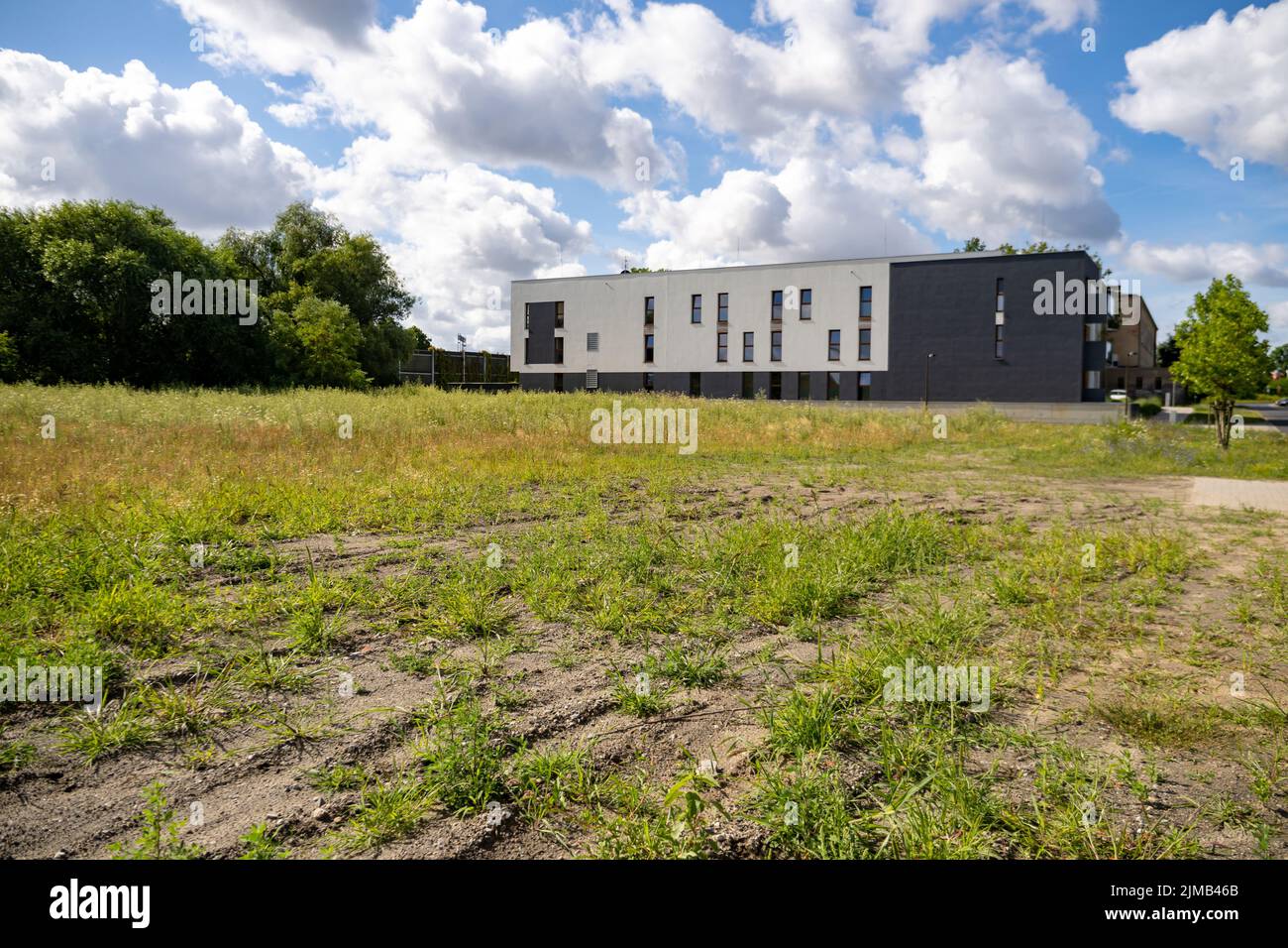 A green weeds field and trees close by an new modern apartment building