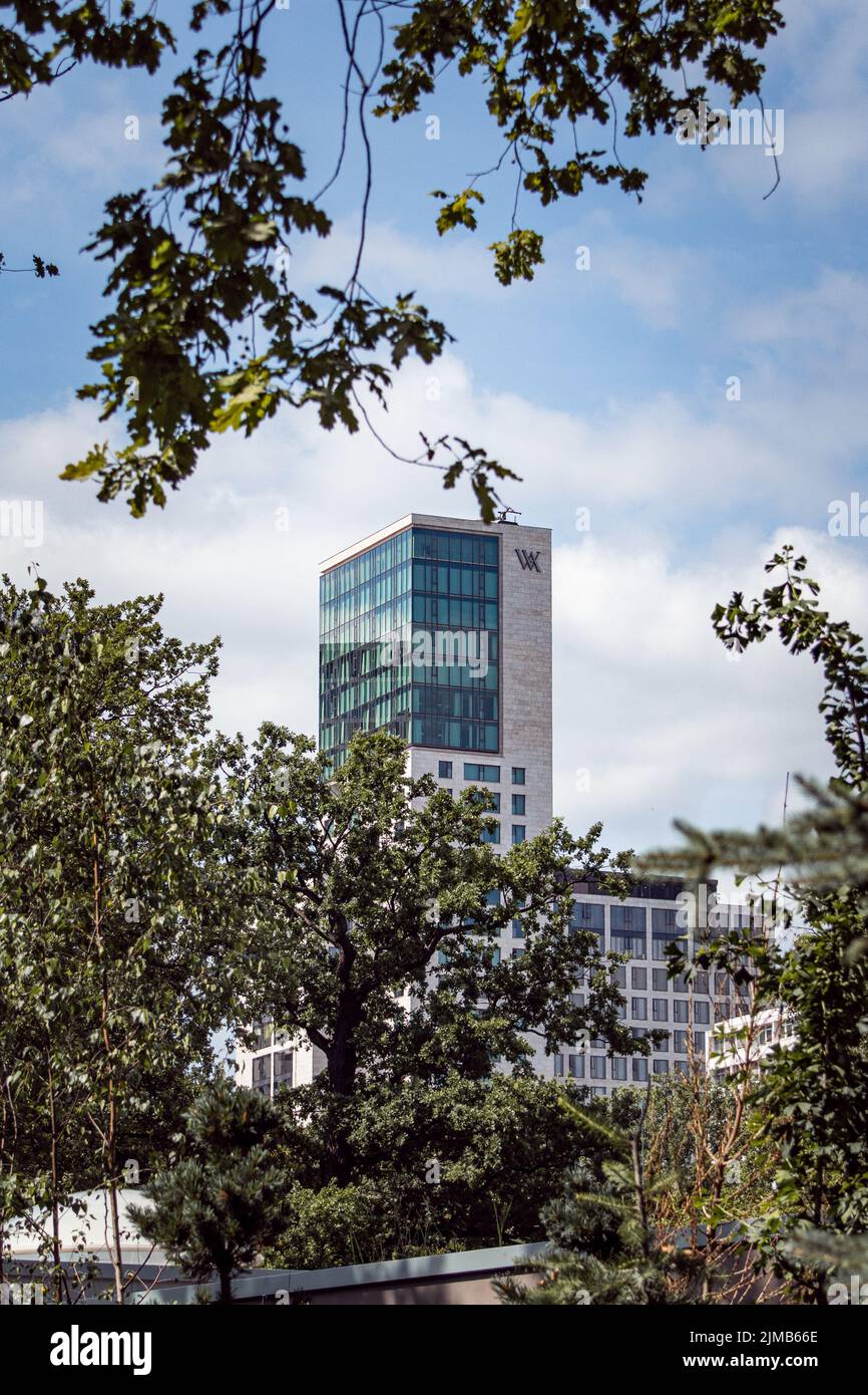 A vertical shot of the Waldorf Astoria Hotel seen behind green tree branches in Berlin, Germany Stock Photo