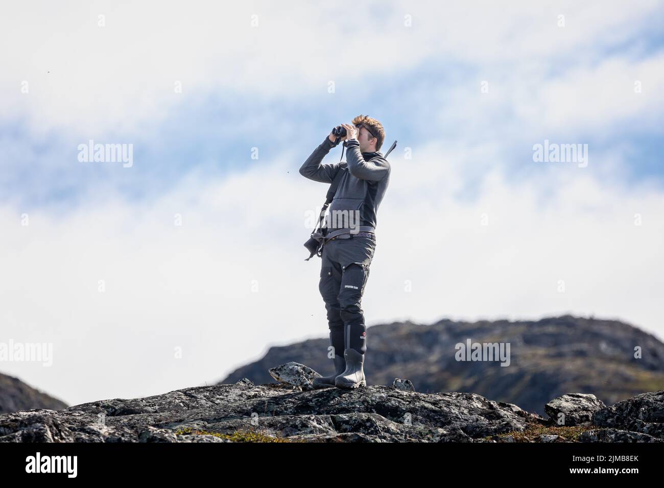 Male lookout armed with rifle scanning for polar bears in the tundra at Ivittuut, Greenland on 21 July 2022 Stock Photo