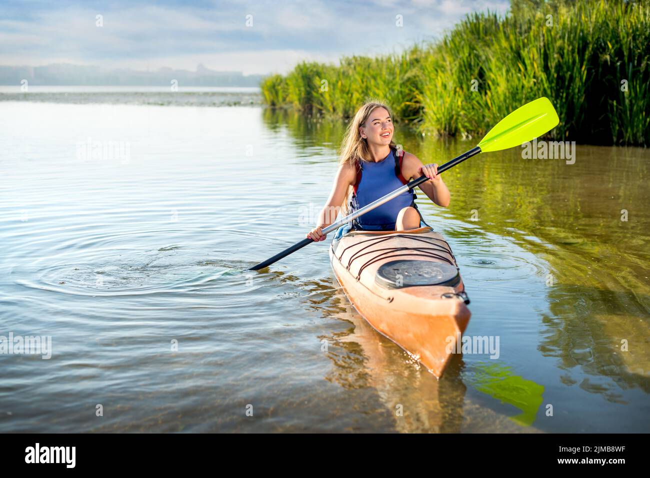 young attractive woman paddling a kayak on a lake with reeds. A girl in