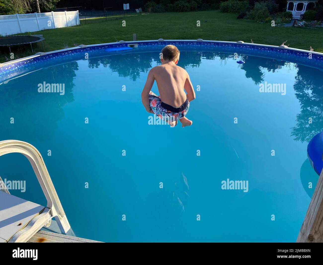 A teenage boy jumping right into the swimming pool with bent knees Stock Photo
