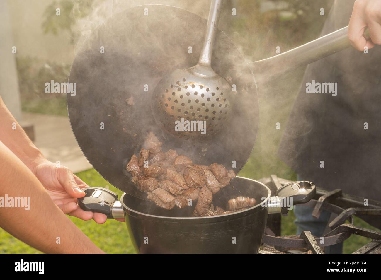 Cropped photo of the hands of men cooking meat in a garden with a portable stove Stock Photo