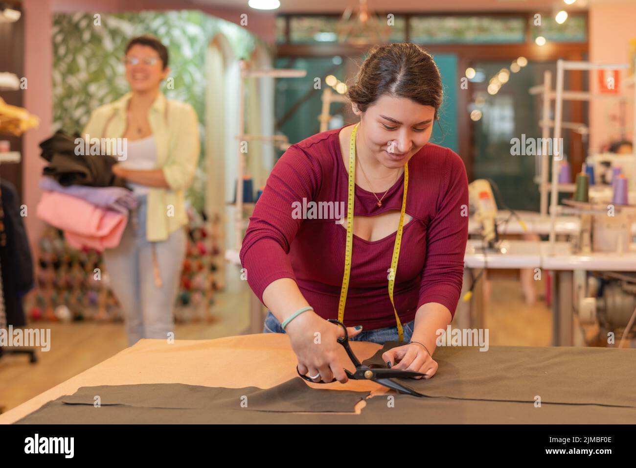 Smiley woman using a scissors to cut a piece of clothes in a sewing ...