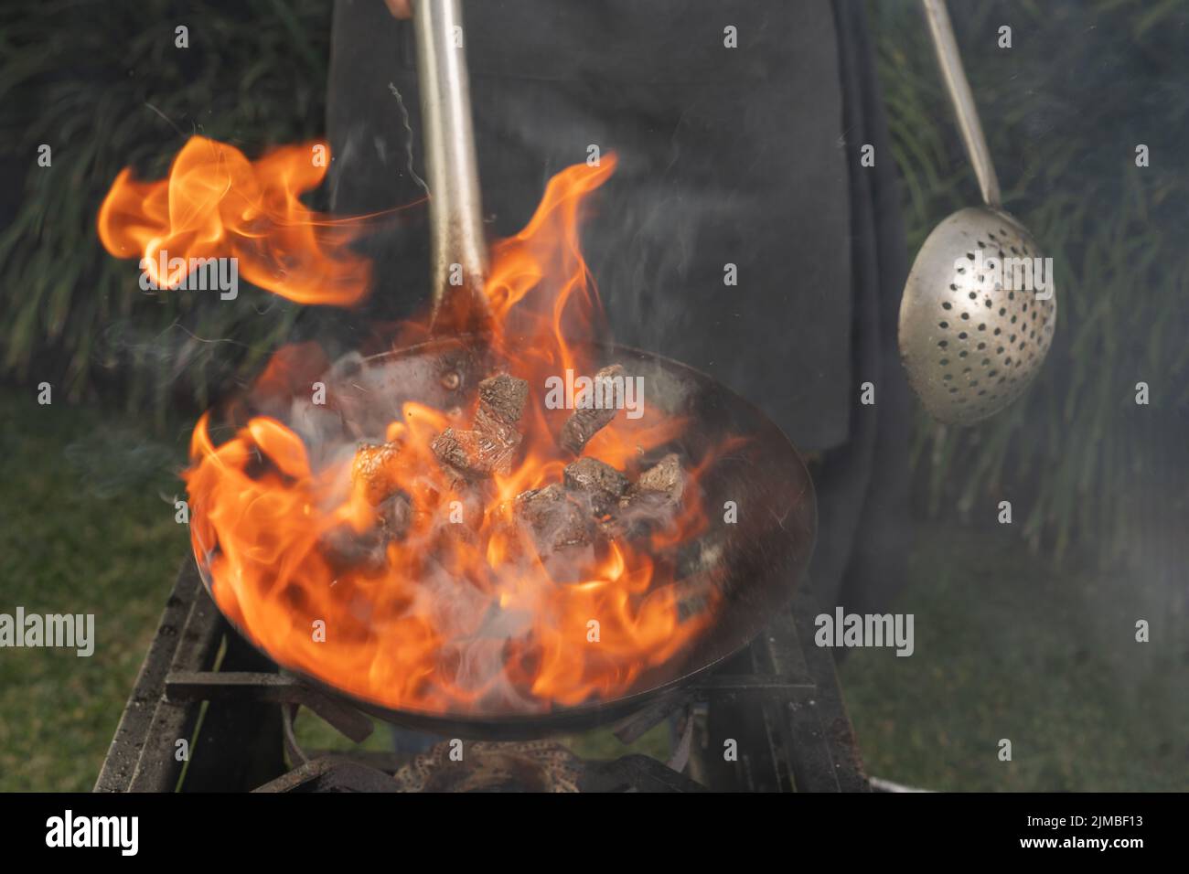 Unrecognizable person flaming meat in a garden using a portable stove and a pan Stock Photo