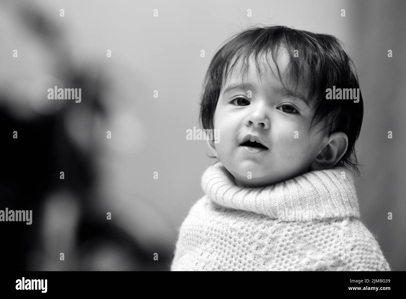 A greyscale shot of a cute 13 months old Indian baby girl wearing a poncho Stock Photo