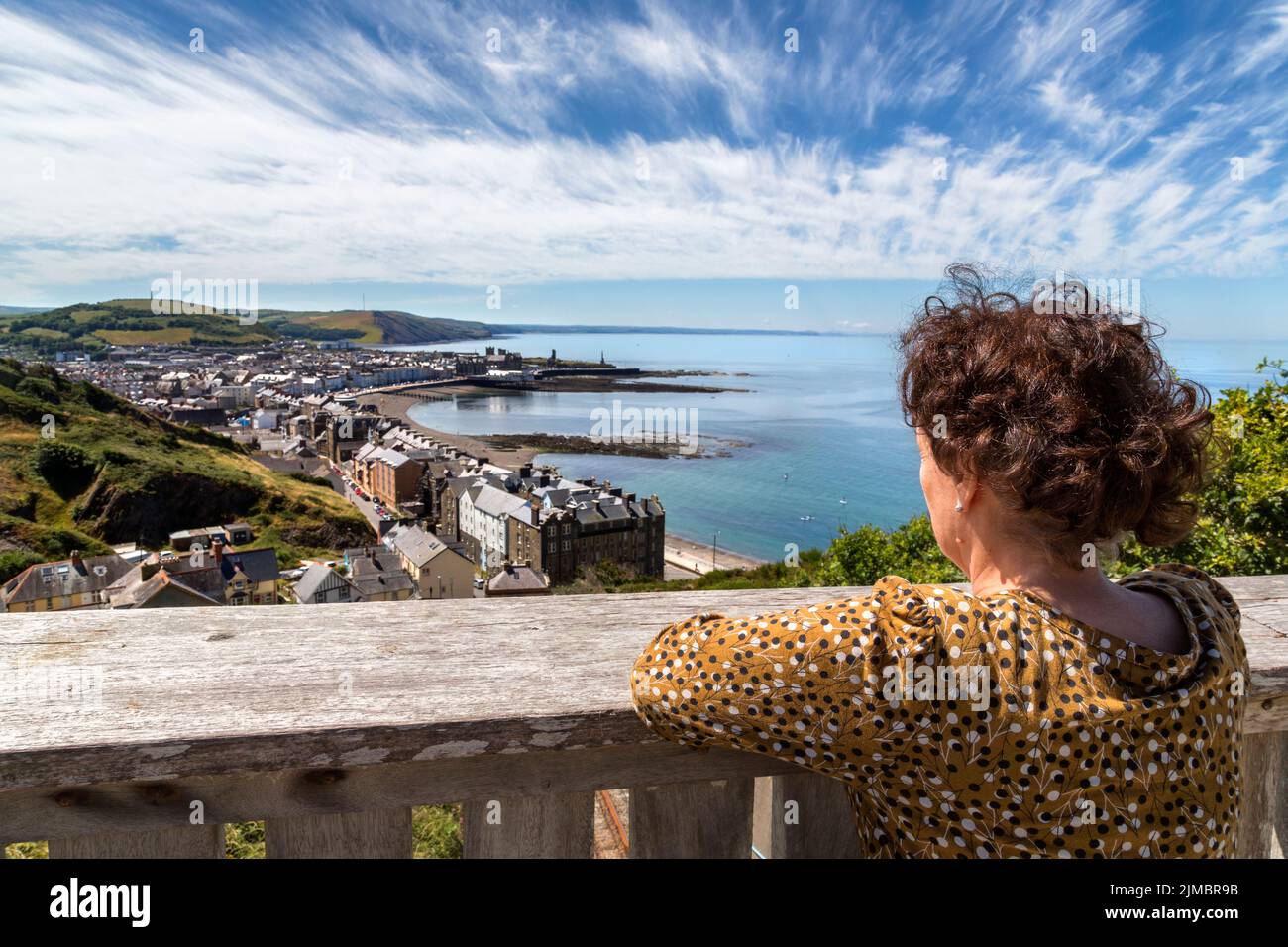 A woman takes in a glorious view of Aberystwyth and Cardigan Bay from a vantage point on Constitution Hill, Wales, UK. Travel, tourism concept. Stock Photo